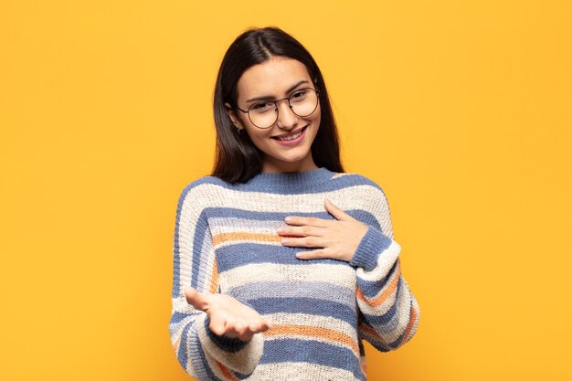 Jeune femme hispanique se sentir heureuse et amoureuse, souriant d'une main à côté du cœur et de l'autre tendue à l'avant