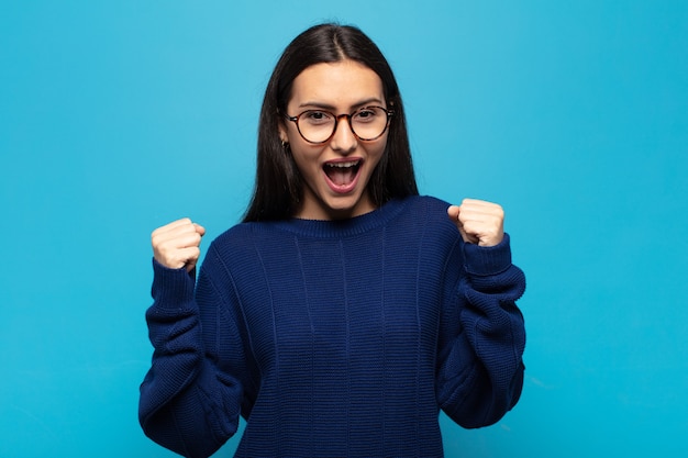 Jeune femme hispanique se sentir heureuse, surprise et fière, criant et célébrant le succès avec un grand sourire