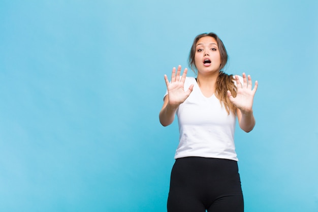 Jeune femme hispanique se sentir stupéfaite et effrayée, craignant quelque chose d'effrayant, avec les mains ouvertes à l'avant en disant rester à l'écart