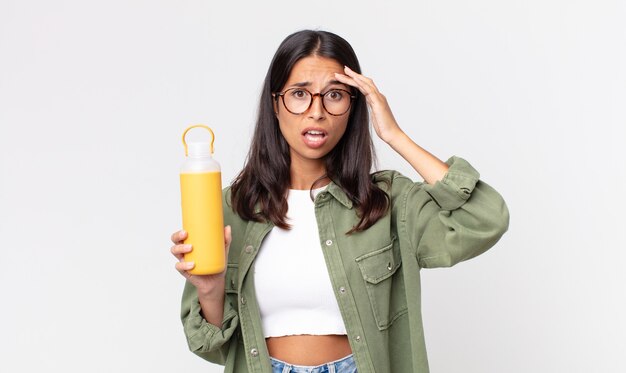 Jeune femme hispanique semblant heureuse, étonnée et surprise et tenant un thermos de café