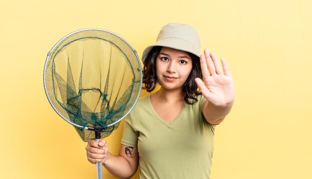 Jeune femme hispanique à la sérieuse montrant la paume ouverte faisant un geste d'arrêt. concept de filet de pêcheur