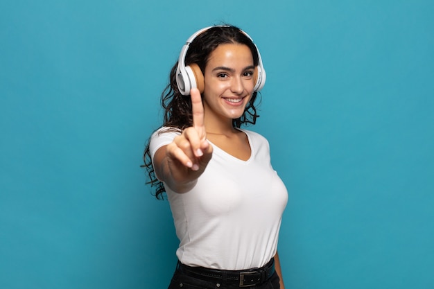 Jeune femme hispanique souriant fièrement et en toute confiance faisant le numéro un pose triomphalement, se sentant comme un leader