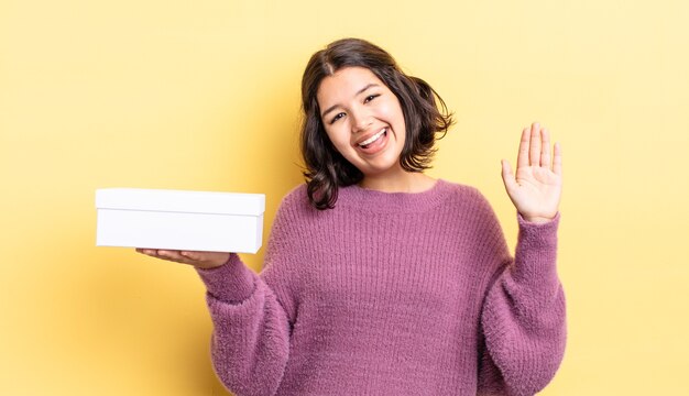 Jeune femme hispanique souriant joyeusement, agitant la main, vous accueillant et vous saluant. concept de boîte vide