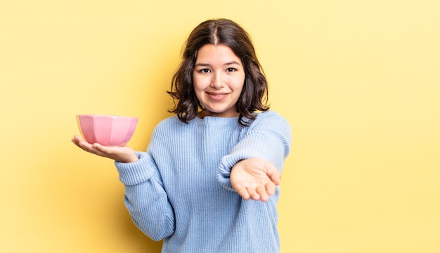 Jeune femme hispanique souriant joyeusement avec amicale et offrant et montrant un concept. concept de bol vide