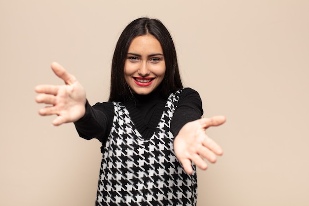 Jeune femme hispanique souriant joyeusement donnant un câlin de bienvenue chaleureux, amical, aimant, se sentir heureux et adorable