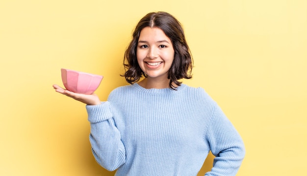 Jeune femme hispanique souriant joyeusement avec une main sur la hanche et confiante. concept de bol vide