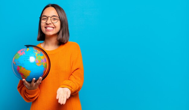 Jeune femme hispanique souriant joyeusement avec un regard amical, confiant et positif, offrant et montrant un objet ou un concept