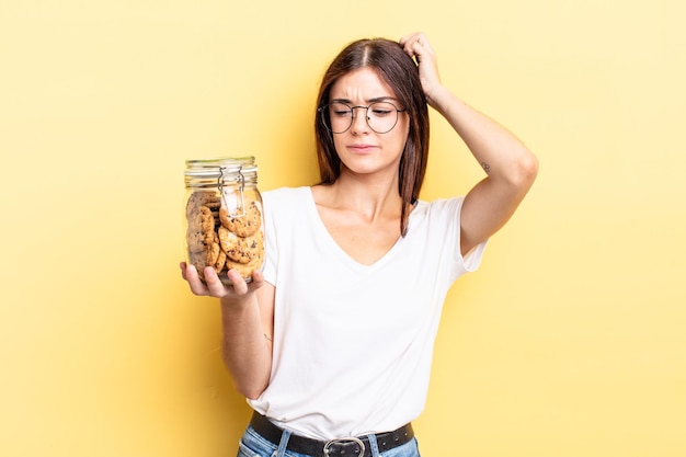 Jeune femme hispanique souriant joyeusement et rêvassant ou doutant du concept de bouteille de biscuits