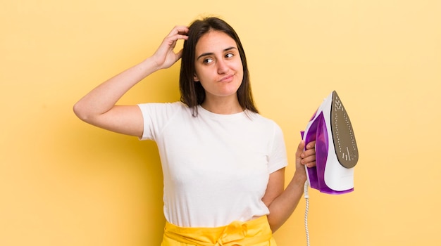 Jeune femme hispanique souriant joyeusement et rêvassant ou doutant du concept de fer à repasser