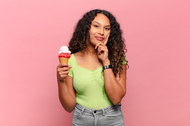 Photo jeune femme hispanique souriant joyeusement et rêvassant ou doutant, regardant sur le côté. concept de crème glacée