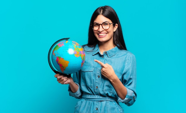 Jeune femme hispanique souriant joyeusement, se sentant heureuse et pointant vers le côté et vers le haut, montrant l'objet dans l'espace de copie. concept de planète terre