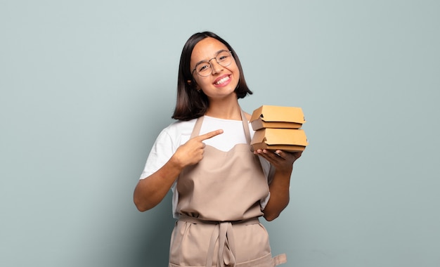 Jeune femme hispanique souriant joyeusement, se sentant heureuse et pointant vers le côté et vers le haut, montrant l'objet dans l'espace de copie