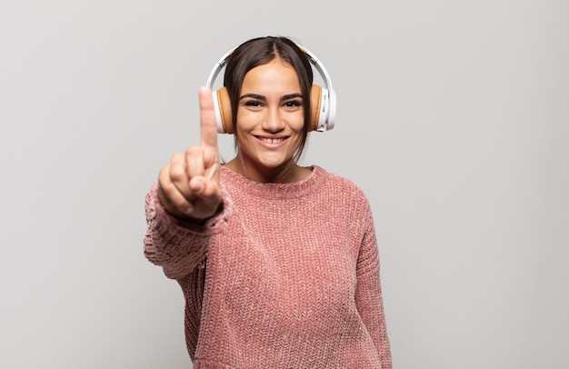 Jeune femme hispanique souriant et à la sympathique, montrant le numéro un ou d'abord avec la main en avant, compte à rebours