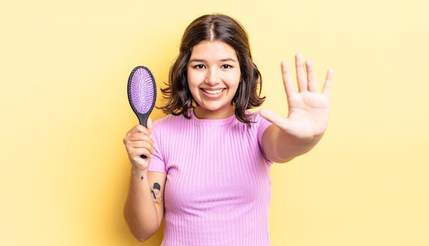 Jeune femme hispanique souriante et amicale, montrant le numéro cinq. concept de brosse à cheveux