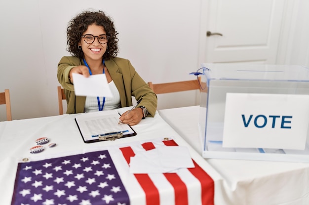 Jeune femme hispanique souriante confiante tenant le vote travaillant au collège électoral