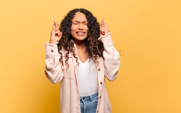 Jeune femme hispanique souriante et croisant anxieusement les deux doigts, se sentant inquiète et souhaitant ou espérant bonne chance