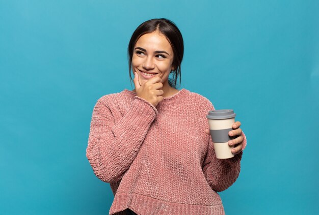 Jeune femme hispanique souriante avec une expression heureuse et confiante avec la main sur le menton, se demandant et regardant sur le côté