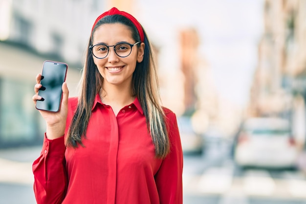 Jeune femme hispanique souriante heureuse montrant un smartphone à écran à la ville