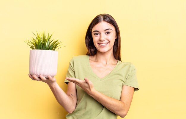 Jeune femme hispanique souriante joyeusement, se sentant heureuse et montrant un concept. concept de pot de plante