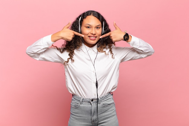 Photo jeune femme hispanique souriante pointant avec confiance vers son propre large sourire, attitude positive, détendue et satisfaite. concept de télévendeur