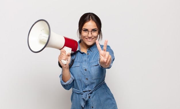 Jeune femme hispanique souriante et à la recherche heureuse, insouciante et positive, gesticulant la victoire ou la paix d'une main