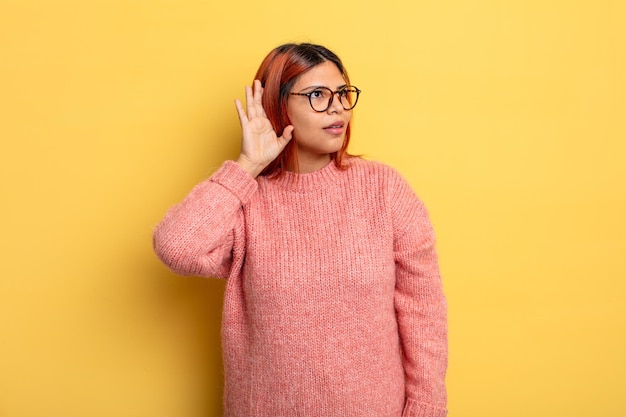 Jeune femme hispanique souriante, regardant curieusement sur le côté, essayant d'écouter des ragots ou d'entendre un secret