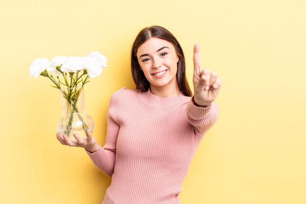 Jeune femme hispanique souriante et semblant amicale, montrant le numéro un. concept de pot de fleur