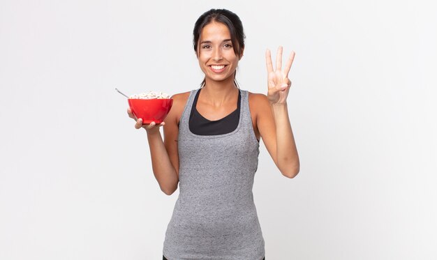 Jeune femme hispanique souriante et semblant amicale, montrant le numéro trois. régime de remise en forme et concept de petit-déjeuner