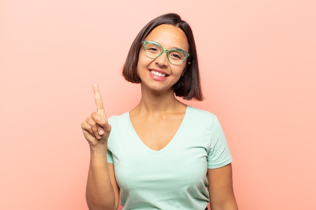 Jeune femme hispanique souriante et à la sympathique, montrant le numéro un ou d'abord avec la main vers l'avant, compte à rebours