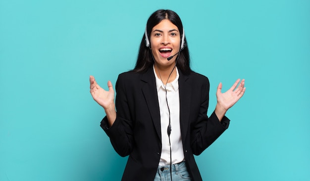 Jeune femme hispanique de télévendeur se sentant heureuse, excitée, surprise ou choquée, souriante et étonnée de quelque chose d'incroyable