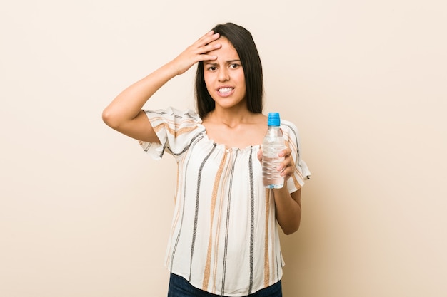 Jeune femme hispanique tenant une bouteille d'eau choquée, elle s'est souvenue d'une réunion importante.