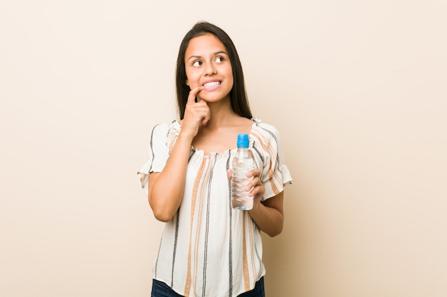 Jeune femme hispanique tenant une bouteille d'eau détendue en pensant à quelque chose en regardant un espace copie.