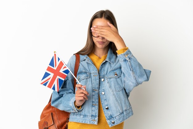 Jeune femme hispanique tenant un drapeau du Royaume-Uni sur fond blanc isolé couvrant les yeux par les mains. Je ne veux pas voir quelque chose