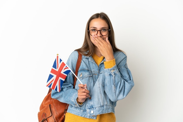 Jeune femme hispanique tenant un drapeau du Royaume-Uni sur fond blanc isolé heureux et souriant couvrant la bouche avec la main