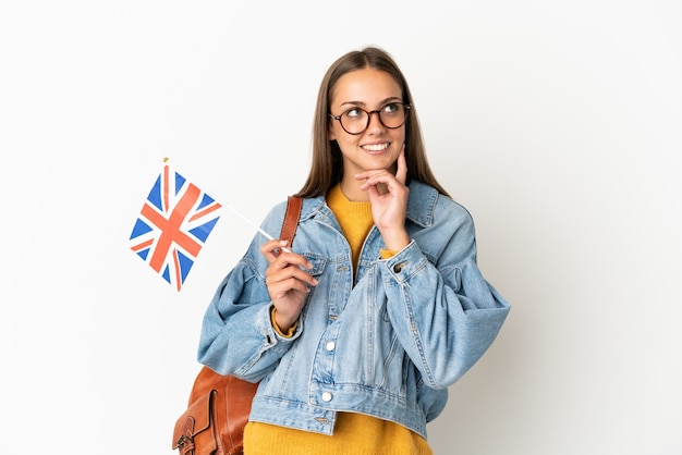 Jeune femme hispanique tenant un drapeau du Royaume-Uni sur fond blanc isolé en pensant à une idée tout en regardant