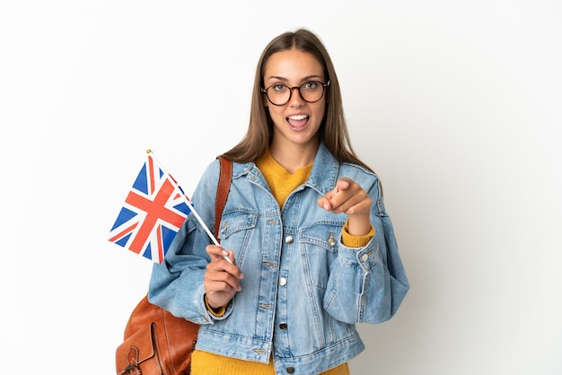 Jeune femme hispanique tenant un drapeau du Royaume-Uni sur fond blanc isolé surpris et pointant vers l'avant