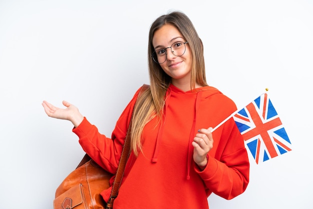 Jeune femme hispanique tenant un drapeau du Royaume-Uni isolé sur fond blanc tendant les mains sur le côté pour inviter à venir