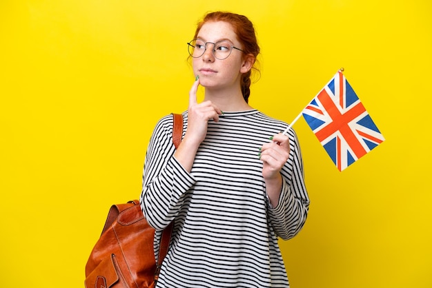 Jeune femme hispanique tenant un drapeau du Royaume-Uni isolé sur fond jaune ayant des doutes en levant les yeux