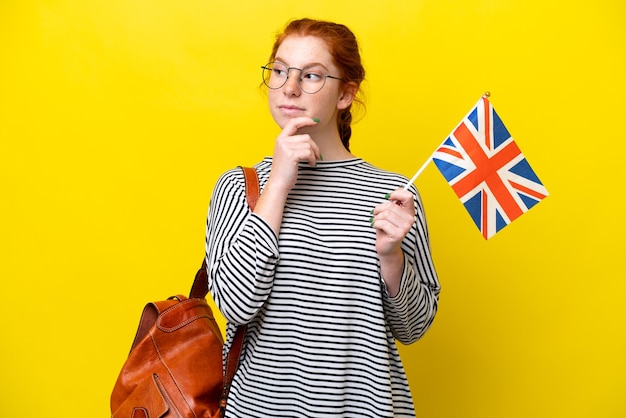 Jeune femme hispanique tenant un drapeau du Royaume-Uni isolé sur fond jaune ayant des doutes