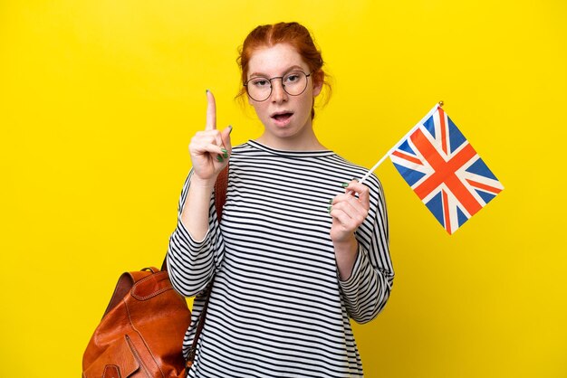 Jeune femme hispanique tenant un drapeau du Royaume-Uni isolé sur fond jaune dans l'intention de réaliser la solution tout en levant un doigt