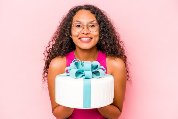 Jeune femme hispanique tenant un gâteau isolé sur fond rose