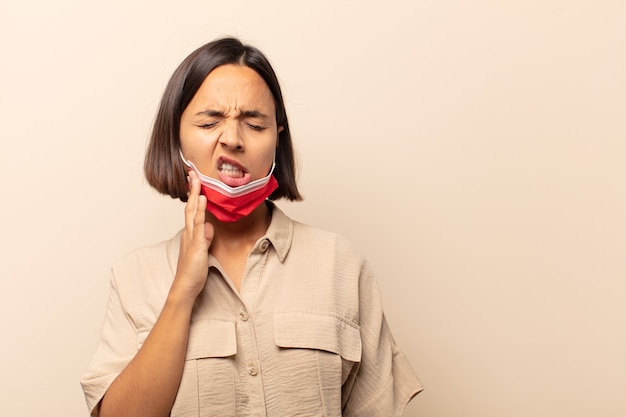 Jeune femme hispanique tenant la joue et souffrant de maux de dents douloureux, se sentir malade, misérable et malheureux, à la recherche d'un dentiste