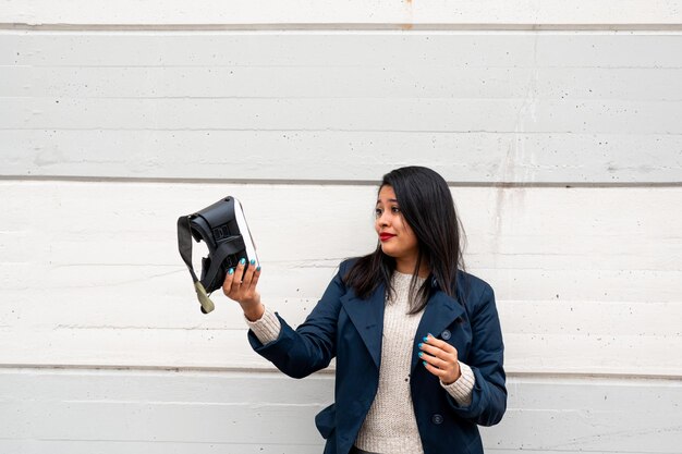 Jeune femme hispanique tenant des lunettes de réalité virtuelle et regardant les lunettes avec un visage inquiet