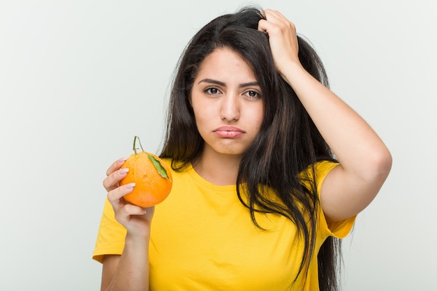 Jeune femme hispanique tenant une orange en état de choc, elle s'est souvenue d'une réunion importante.