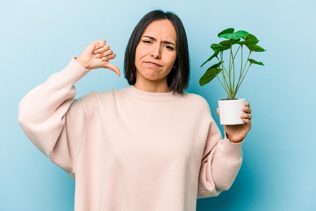 Jeune femme hispanique tenant une plante isolée sur fond bleu se sent fier et confiant exemple à suivre