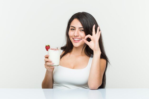 Jeune femme hispanique tenant un smoothie jeune femme hispanique tenant un toast à l'avocat, gai et confiant, montrant le geste correct. <Mixto>