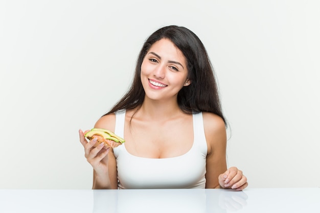 Jeune femme hispanique tenant un toast à l'avocat heureux, souriant et gai.