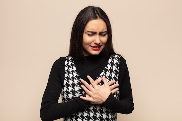 Jeune femme hispanique à la triste, blessée et le cœur brisé, tenant les deux mains près du cœur, pleurant et se sentant déprimé