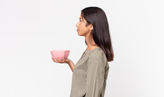 Jeune femme hispanique en vue de profil pensant, imaginant ou rêvant et tenant un bol ou un pot vide