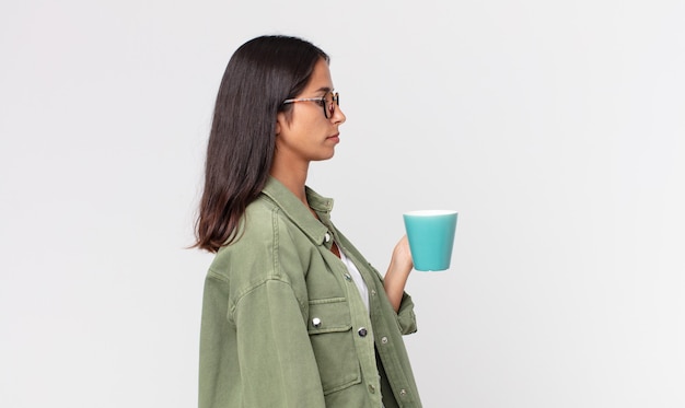 Jeune femme hispanique sur la vue de profil pensant, imaginant ou rêvant et tenant une tasse de café